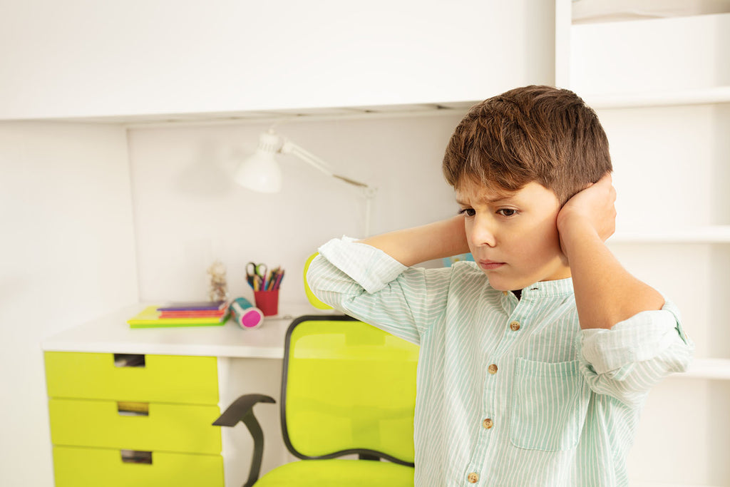 Young boy with ASD is sad while covering ears after being overwhelmed.